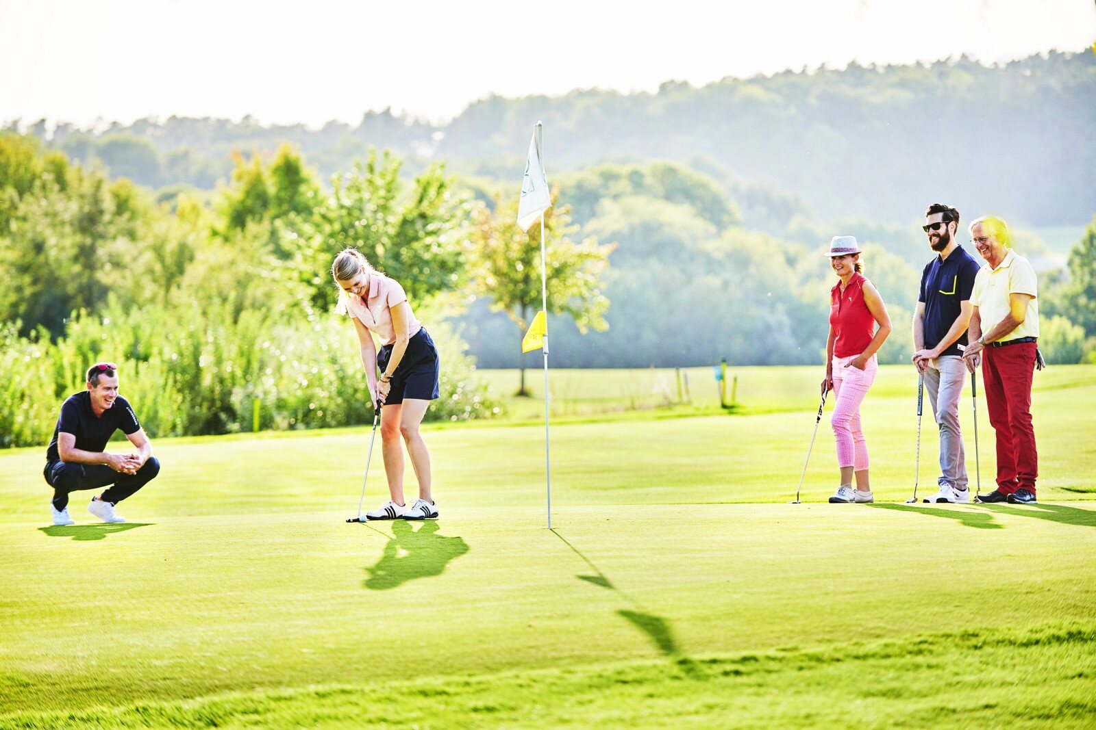 Eine Gruppe von Golferinnen und Golfern begleitet eine Spielerin auf dem Putting Green.